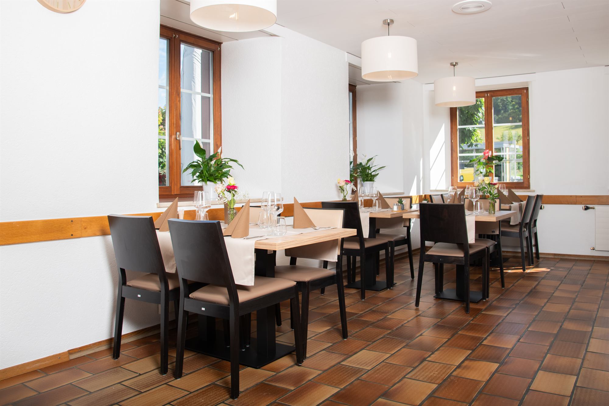 Heller Restaurantsaal mit weissen Wänden, gedeckten Tischen und Terrakotta-Boden.